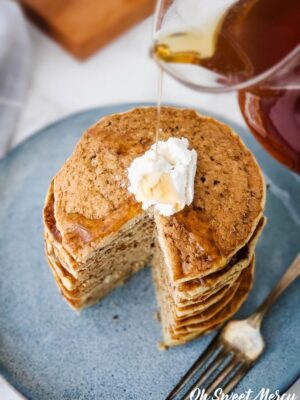 Pouring syrup over stack of Millet Pancakes with vegan butter on blue plate