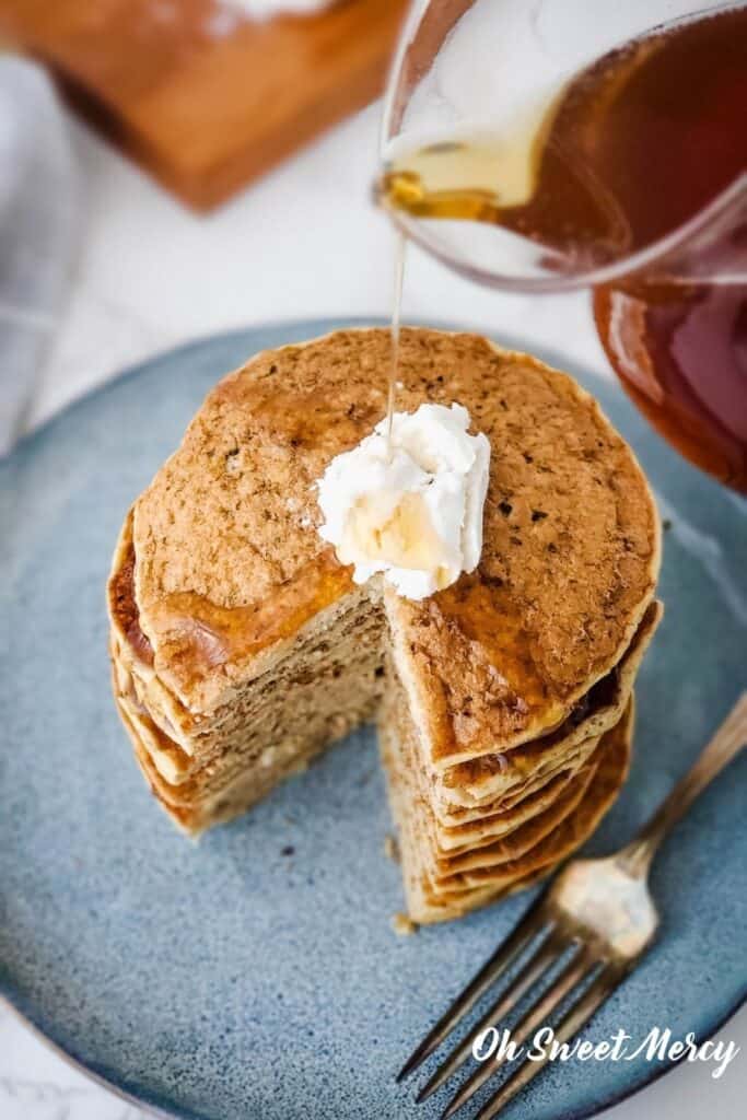 Pouring syrup over stack of Millet Pancakes with vegan butter on blue plate