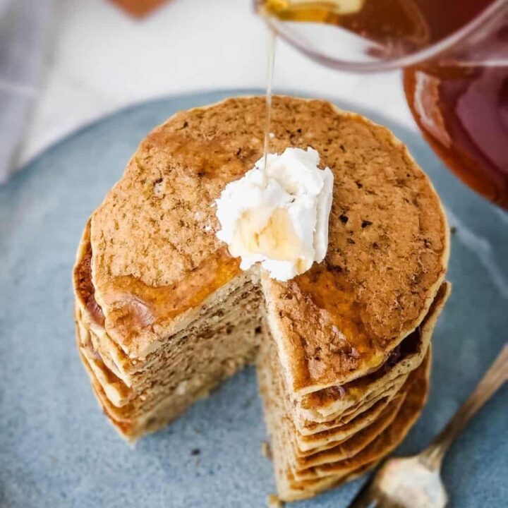 Pouring syrup over stack of Millet Pancakes with vegan butter on blue plate
