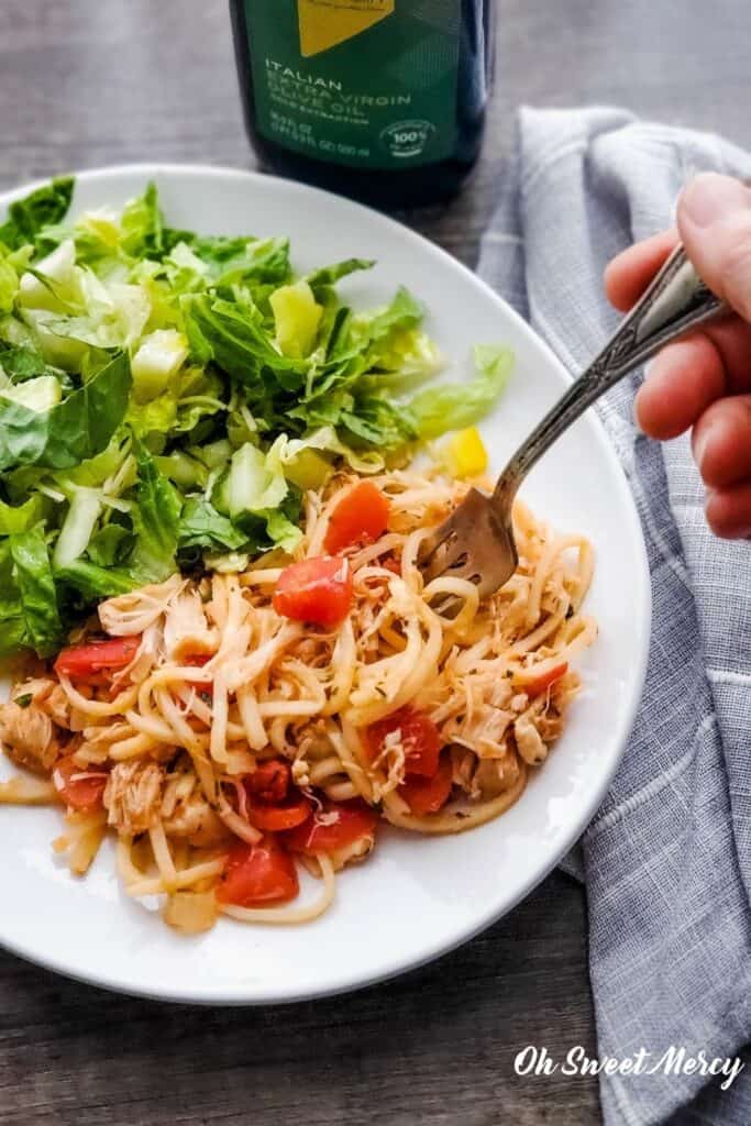 Plate of hearts of palm pasta, chicken, and a tomato sauce made with 100% Italian extra virgin olive oil, with salad, bottle of oil in background