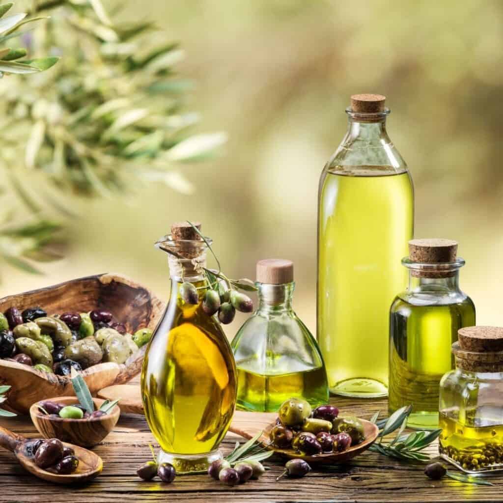 several bottles of olive oils with olives, olive tree in background