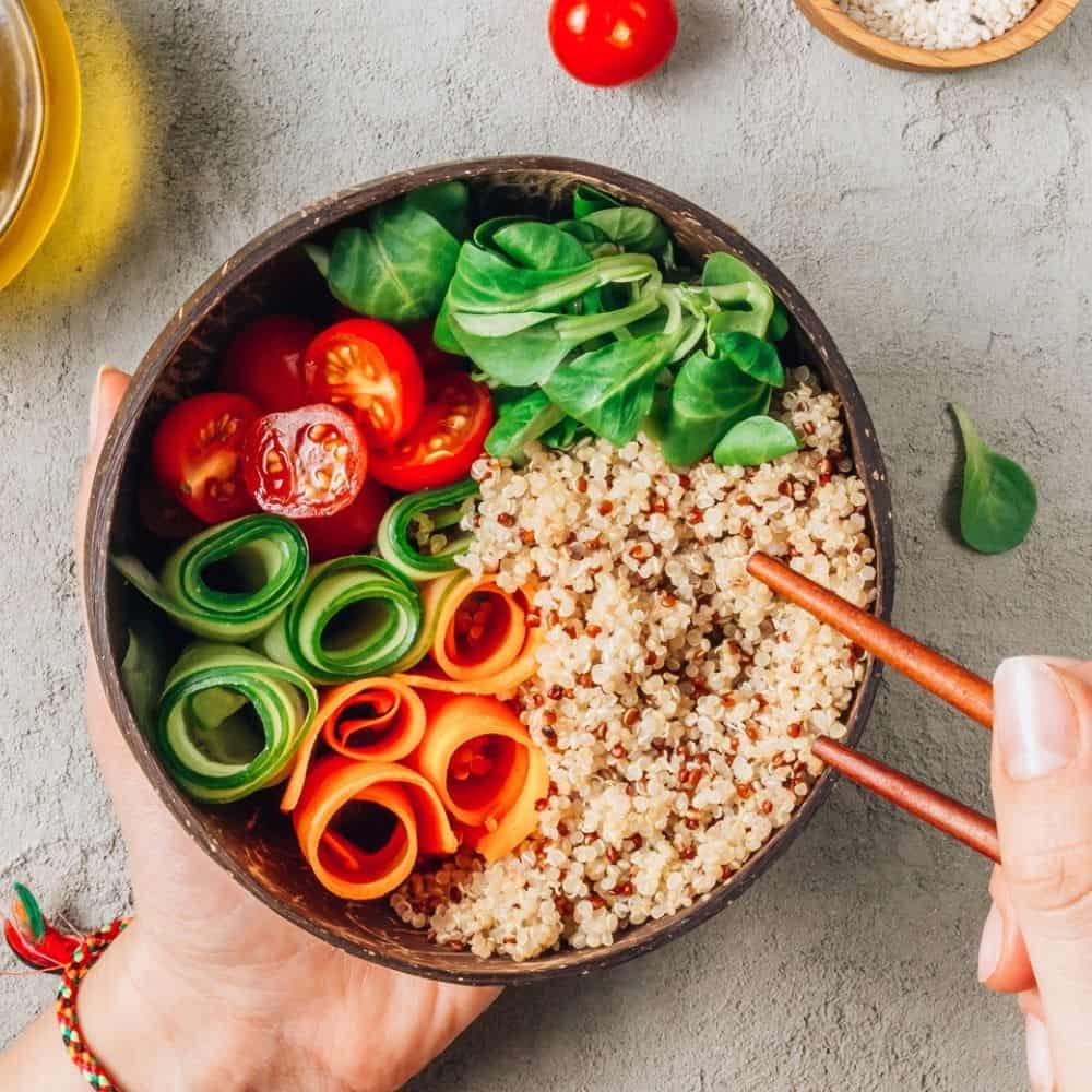 quinoa grain bowl with veggies, woman holding chopsticks in bowl