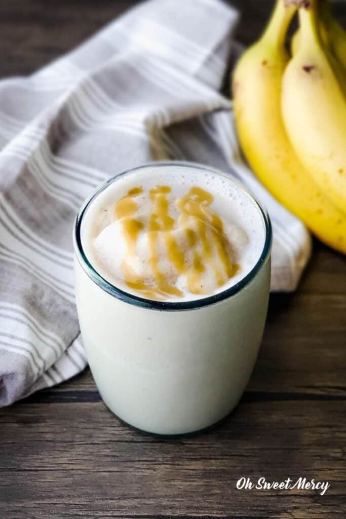 Glass of Banana Maple Tahini Smoothie with kitchen towel and bananas in the background