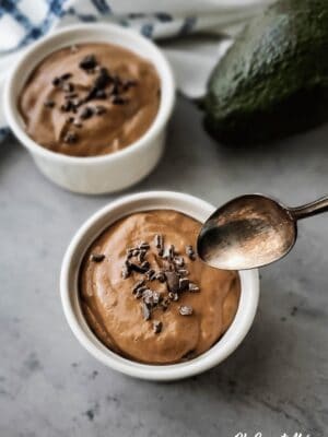 Small white bowls of pudding with raw cacao nibs sprinkled on top, a spoon hovering over one of the bowls