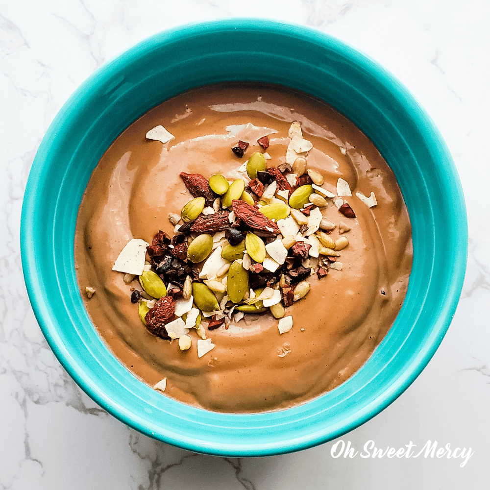 Bowl of Chocolate Protein Pudding with trail mix sprinkled on top - nuts, seeds, cacao nibs, goji berries, coconut flakes
