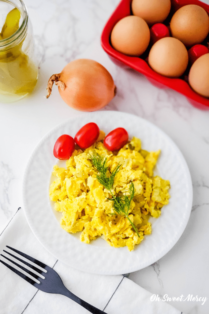 White plate of Dill Pickled Scrambled Eggs garnished with fresh dill and cherry tomatoes